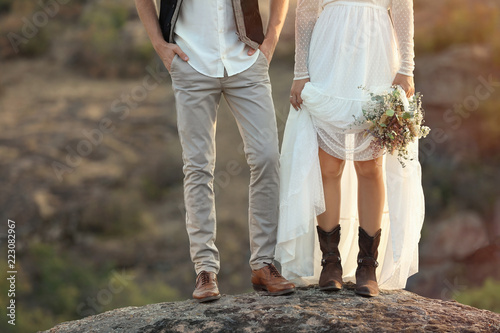 Happy newlyweds with beautiful field bouquet standing on rock outdoors, closeup