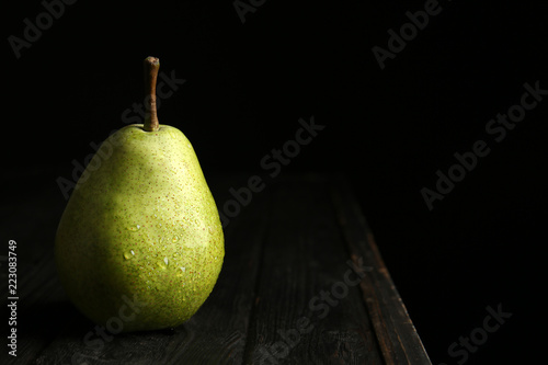 Ripe pear on wooden table against dark background. Space for text