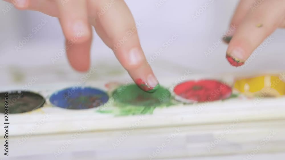 A small child paints with watercolor, wetting his finger in a jar of paint A small child paints with watercolor, wetting his finger in a jar of paint