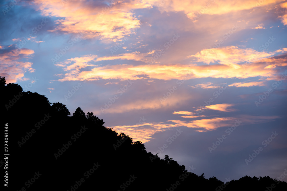 colorful cloudy sky with blue orange and silhouette tree canopy on mountain at bottom