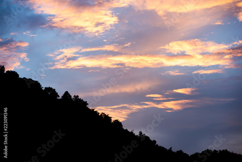 colorful cloudy sky with blue orange and silhouette tree canopy on mountain at bottom