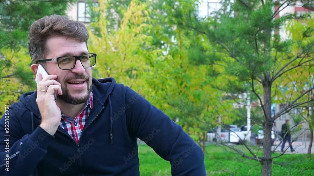Cheerful man sitting in the Park on the bench. Speak by phone.