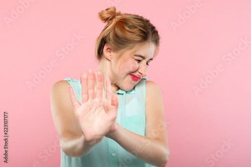 don't want to see it. rejection refusal and denial. young woman putting hands forward as if pushing smth away. portrait of a girl with tightly shut eyes on pink background. photo