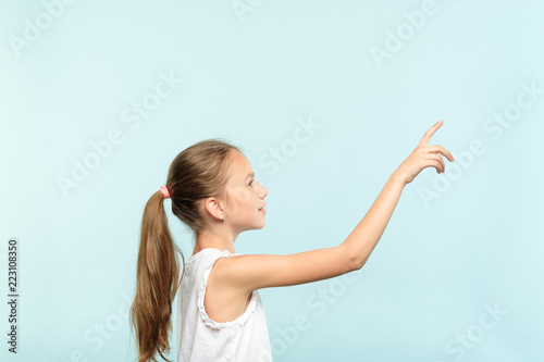 thoughtful girl reaching and wanting to press invisible button on the right. interface or virtual screen concept. free space for advertisement or text. portrait child on blue background.