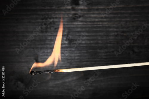 A side view of a burning match, with fire, on a dark background with a place for text
