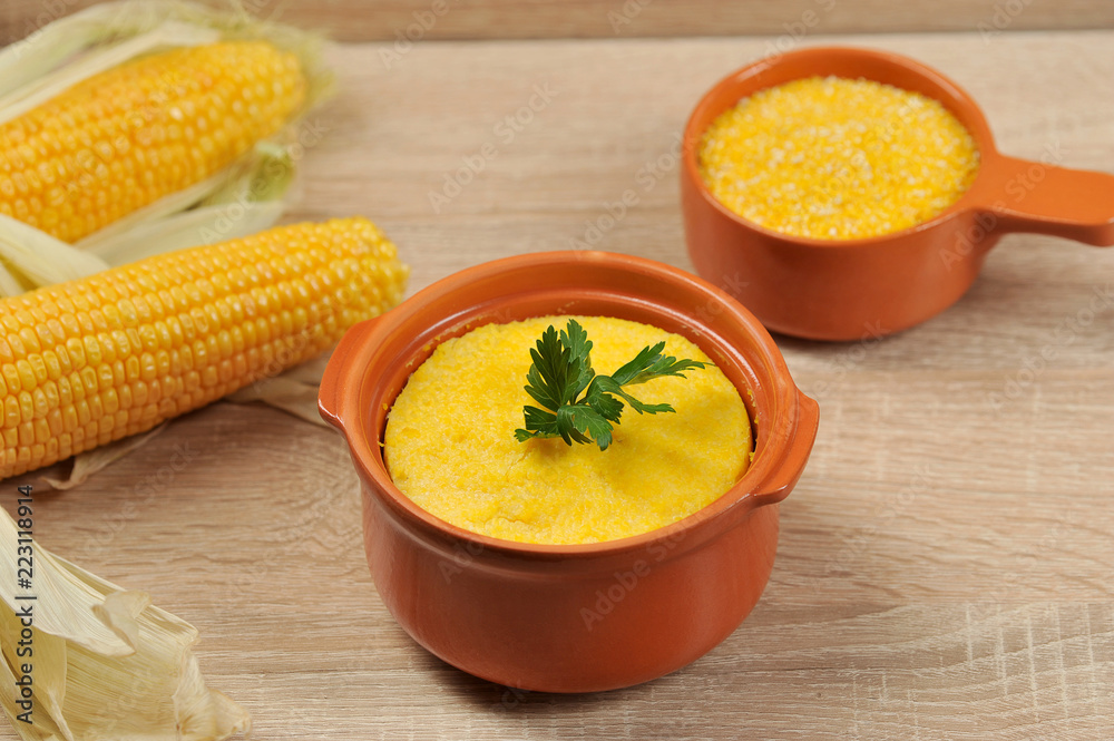 Corn hominy porridge in a clay pot. Corn flour in a clay bowl and cob of ripe corn. Light background. Close-up. View from above. Corn hominy porridge in a clay pot. Corn flour in a clay bowl and cob of ripe corn. Light background. Close-up. View from above.