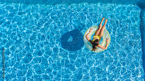 Aerial drone view of little girl in swimming pool from above, kid swims on inflatable ring donut , child has fun in blue water on family vacation resort 