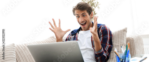 Schilderij op canvas surprised young man with laptop sitting on sofa