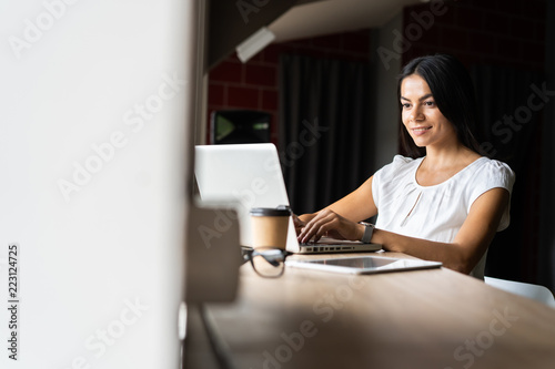 Searching for new solution. Pensive young beautiful businesswoman in glasses working on laptop while sitting at her working place