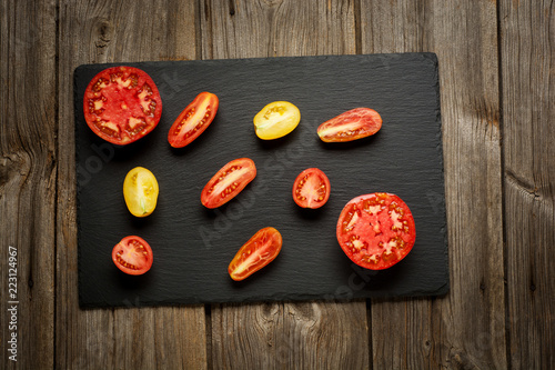 Variety of ripe fresh organic gardening tomatoes different kind and colors with water spot and basil leaves in wood tray over old grey wooden background. Flat lay, space