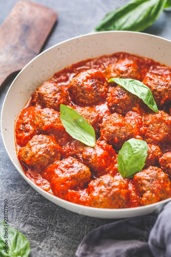 Tasty beef meatballs in tomato sauce with spices and fresh basil on a kitchen table. Food photography, vertical shot, European cuisine.