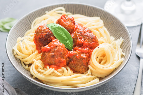Beef meatballs in tomato sauce with Italian spaghetti and fresh basil leaf on a dinner table. Simply homemade recipe, close up.