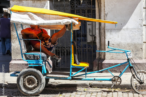 Havana / Cuba - August 15, 2015: Vintage coach strange bicycle with driver resting leg up on it, outdoors, sunny day.