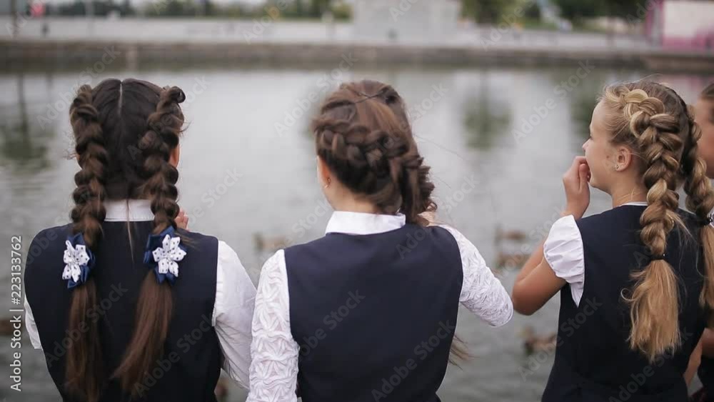 Students in school uniform feeding ducks in a pond in the school yard. Girls College coeds wearing the same school uniform feed the ducks in the pond on campus