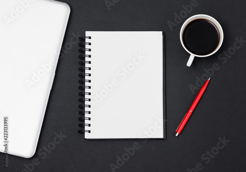 Business flat lay composition  workspace with blank notepad  closed laptop  red pen and coffee cup on black table. Free space for text input. Top view shot. Businessman or student desk.