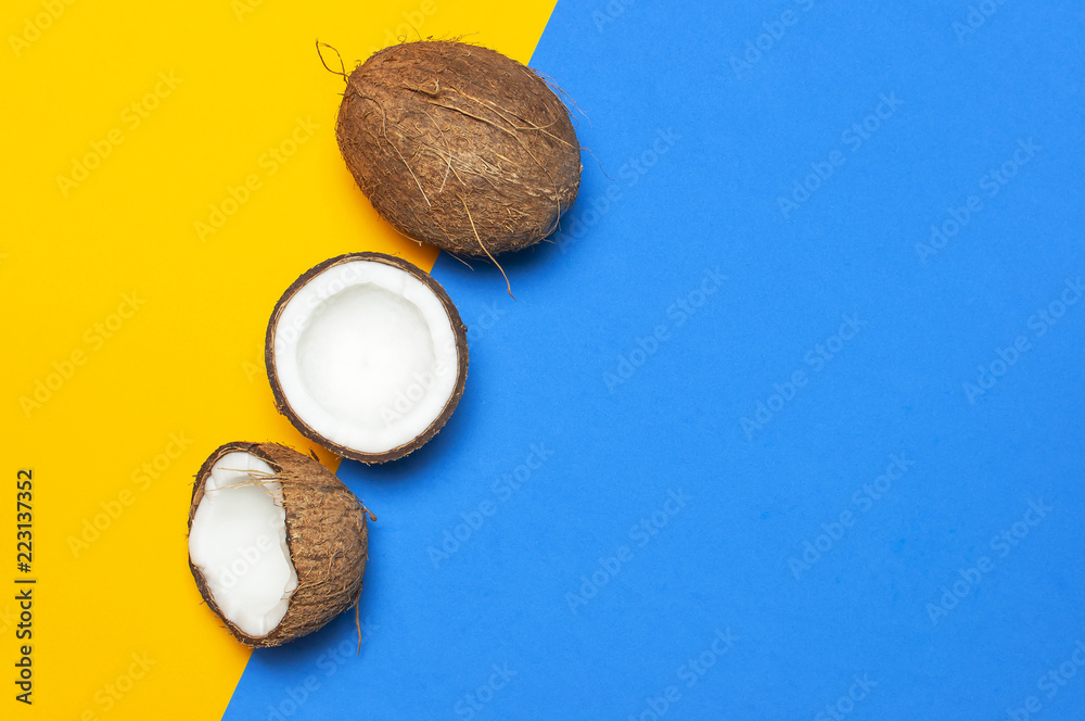 Ripe coconut on yellow and blue colored background, minimal flat lay style top view with copy space. Pop art design, creative summer and food concept. Tropical fruit whole and half abstract background Ripe coconut on yellow and blue colored background, minimal flat lay style top view with copy space. Pop art design, creative summer and food concept. Tropical fruit whole and half abstract background