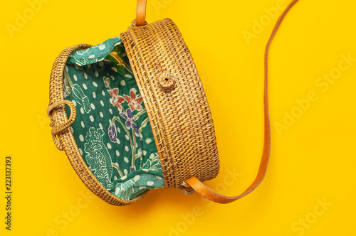 Fashionable handmade natural organic round rattan bag on bright yellow background flat lay. Top view with copy space. Trendy bamboo bag Ecobags from Bali. Summer fashion concept. photo