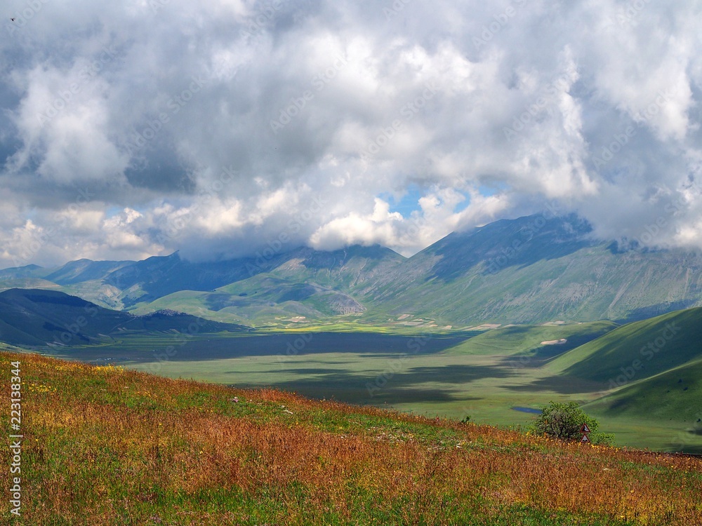 Castelluccio di Norcia, where wide fields, mountains covered with clouds, clouds cast shadows on the ground