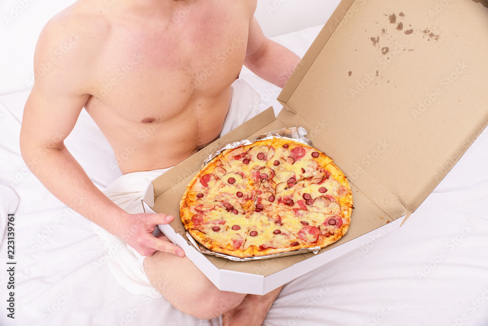 Male courier sexy muscular torso holds pizza. Sexy courier delivers  gastronomic satisfaction to your bed. Guy naked covered pizza box sit bed  bedroom offer you join him. Gastronomic satisfaction Stock Photo