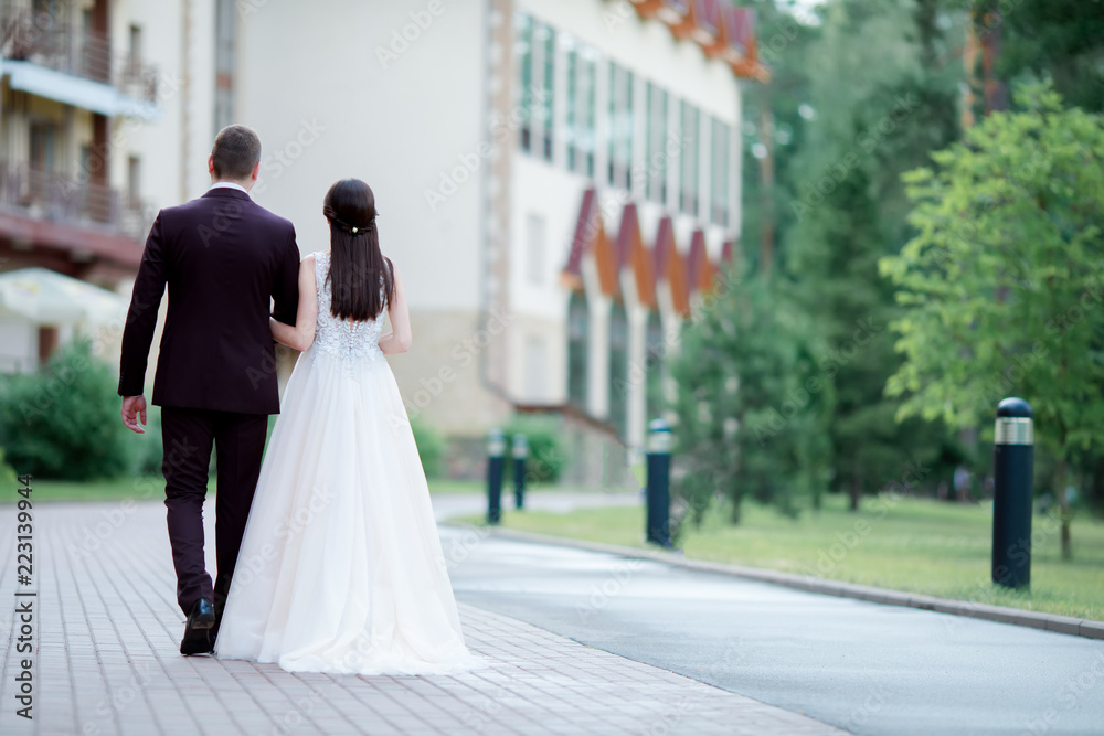 Bride and groom walking away outdoors, hotel territory. Back view.