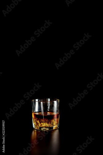 Single glass of whisky or whiskey with ice on black background.