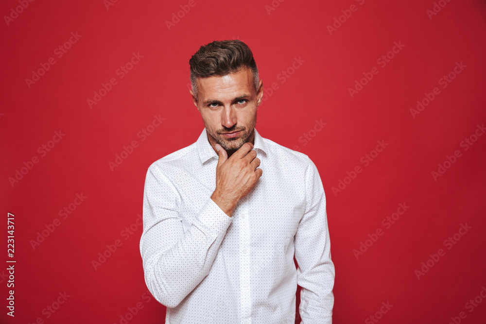 Handsome guy with stubble in white shirt looking on camera, isolated over red background
