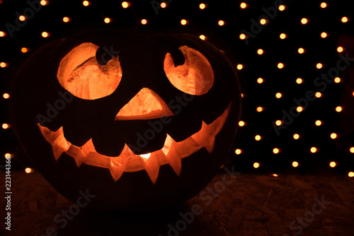 Funny orange pumpkin like a head with eyes and a smile on a black background with a garland for the Halloween party
