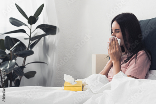 sick young woman with box of paper napkins sitting in bed photo