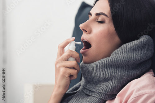 sick young woman in scarf using cough spray