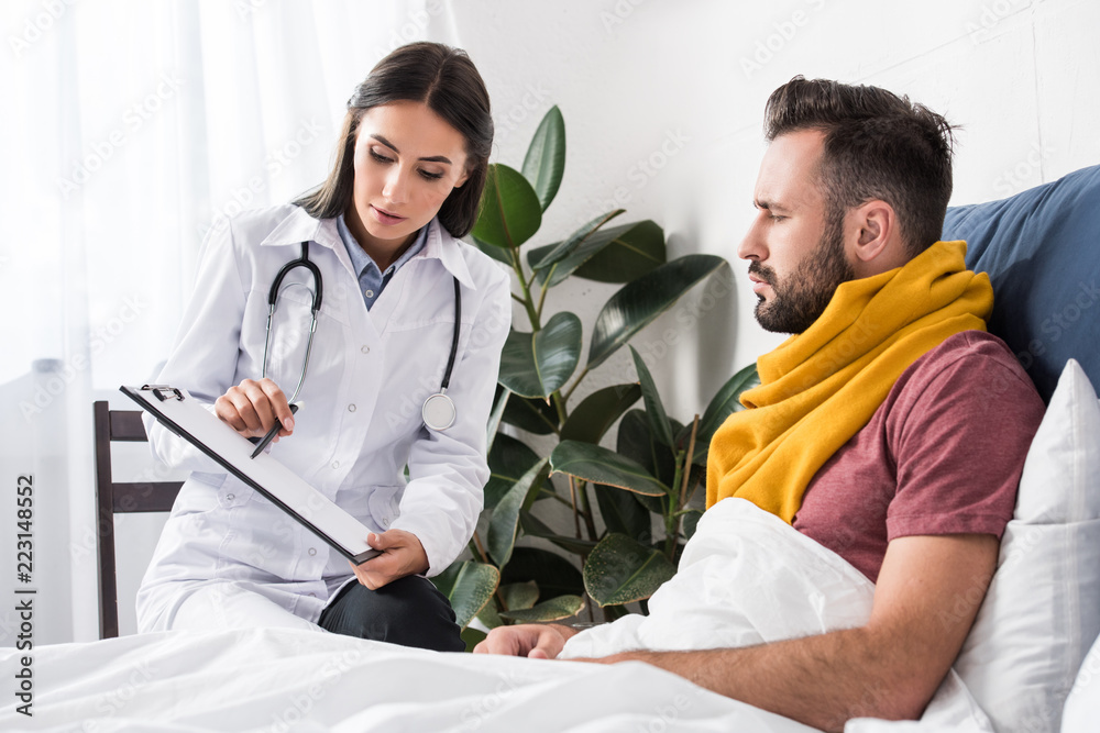 female doctor showing clipboard with documents to patient while lying in bed female doctor showing clipboard with documents to patient while lying in bed