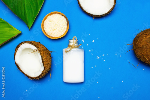 Organic cosmetics with coconut oil, ripe coconut on blue colored background top view minimal flat lay style. Coconut shavings, oil, milk. Healthy skincare. Homemade cosmetic for peeling and spa care.