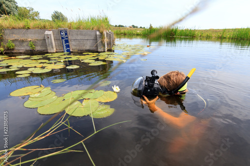 Very handsome young man in a river with water lilies in Rijpwetering, the Netherlands, with equipment for underwater photography on July 19, 2014
