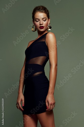 Beautiful young, slender, tanned girl with bright make-up and high hairstyle posing in the studio in a fashionable dress on a gray background.