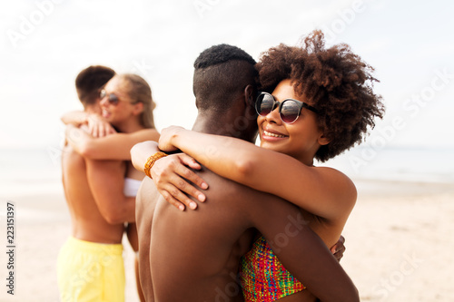 friendship, summer holidays and people concept - happy friends or couples hugging on beach