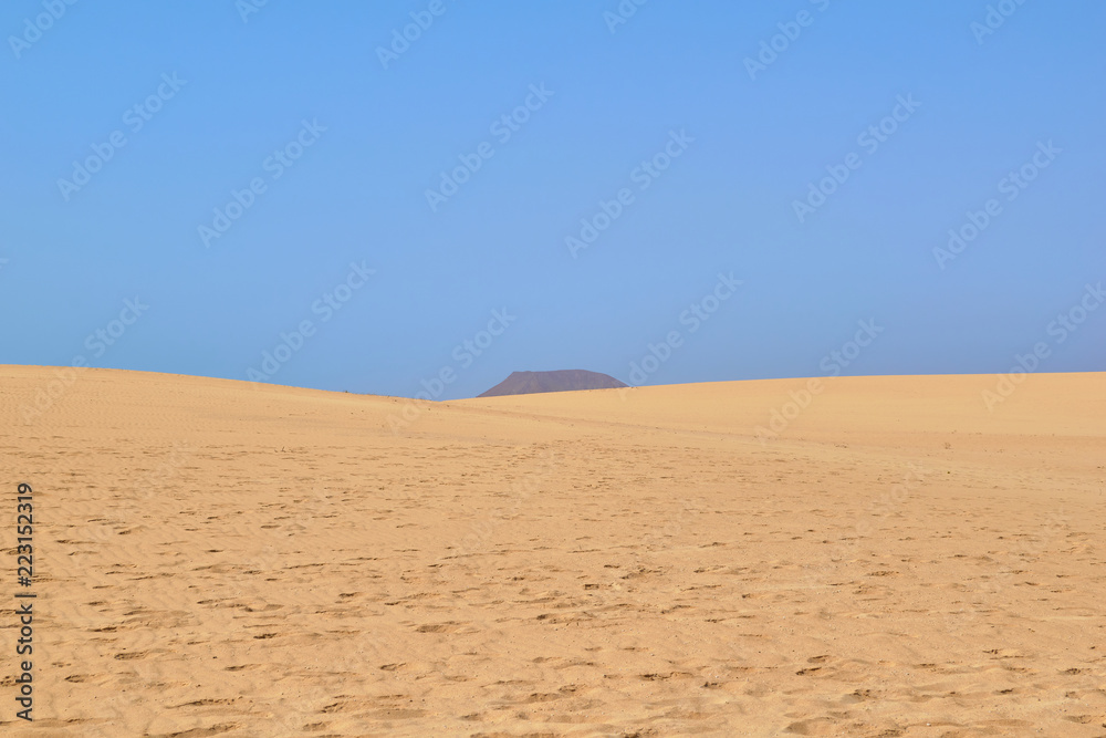 Golden sand landscape with footsteps in the foreground and dark mountain background and blue sky on a clear day Corralejo, Fuerteventura, Canary Islands, Spain