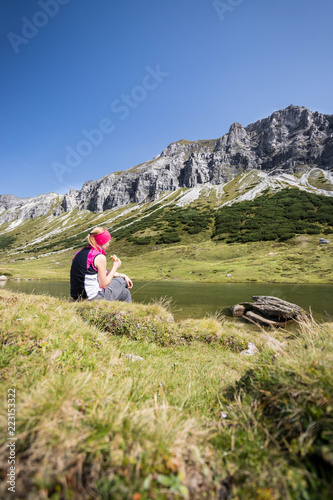 Junge blonde Frau rastet am Ufer eines Bergsees, Österreich