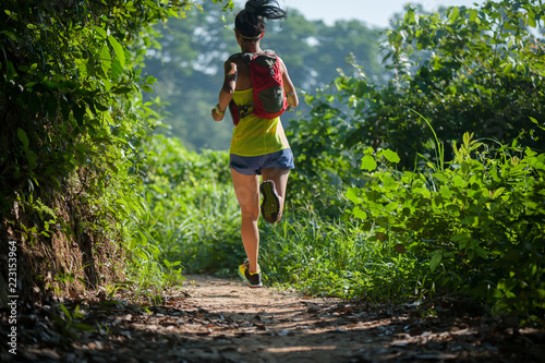 Young woman trail runner running on tropical forest trail during morning