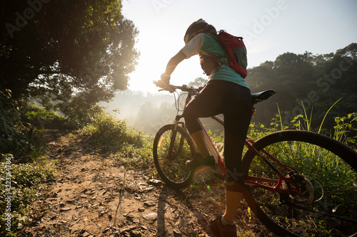 Young woman cyclist riding mountain bike on summer forest trail