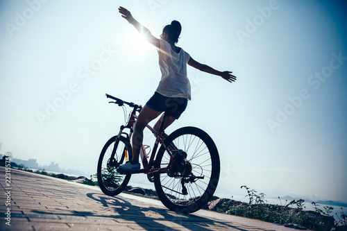 Fotografia Hands free cycling woman riding mountain mike on sunrise seaside