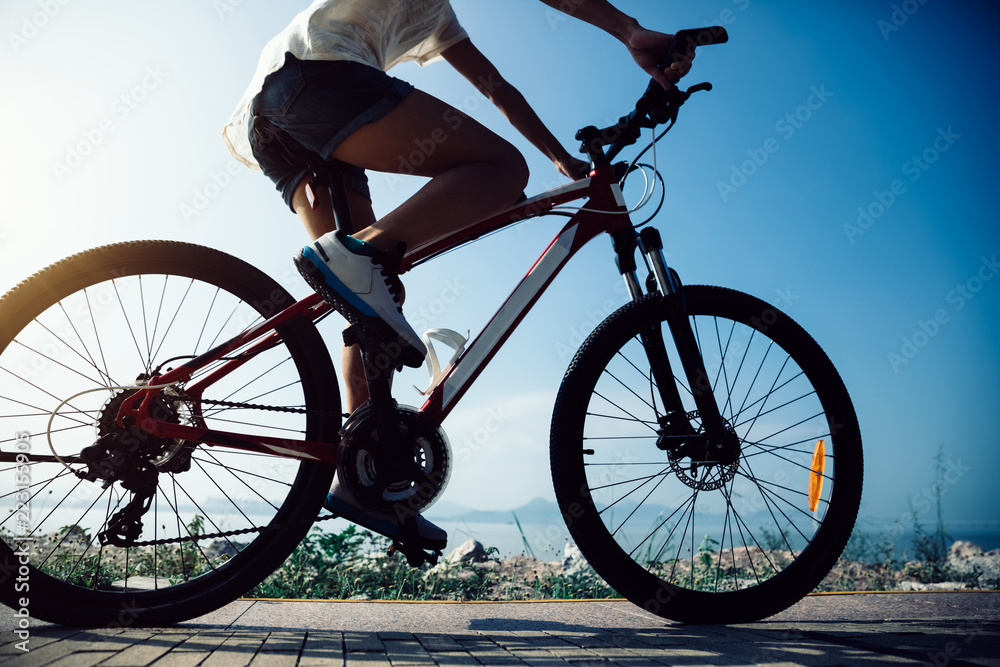 Fototapeta premium Cycling woman riding mountain mike on sunrise seaside