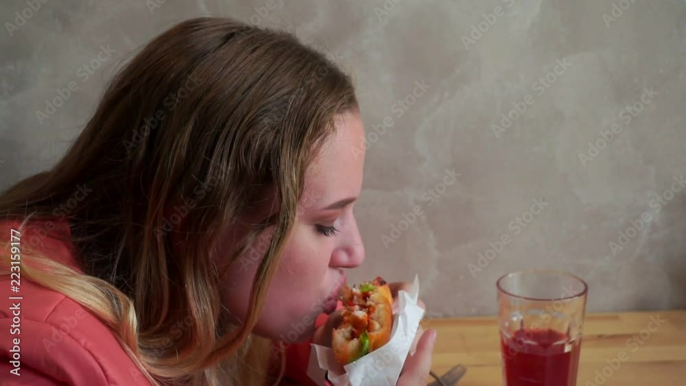 A young hungry girl eating a hamburger. Sitting at a table in a cafe. Slow mo A young hungry girl eating a hamburger. Sitting at a table in a cafe. Slow mo