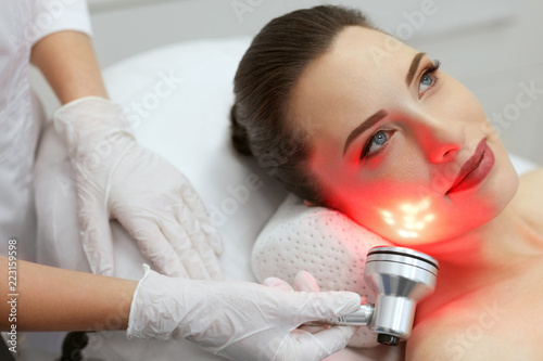 Red Led Light Treatment. Woman Doing Facial Skin Therapy 