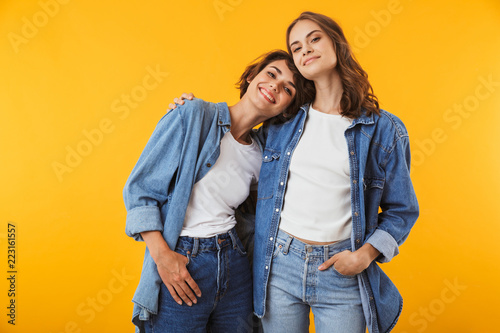 Women friends posing isolated over yellow background.