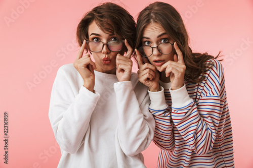 Emotional young women friends posing isolated over pink background.