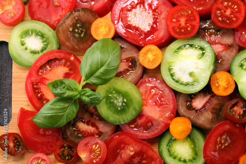 various colorful tomatoes and basil leaves on rustic table.