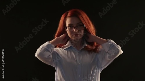 a beautiful girl with red hair in a white shirt posing on a black background in front of the camera. the model advertises glasses, lenses or services to restore vision photo