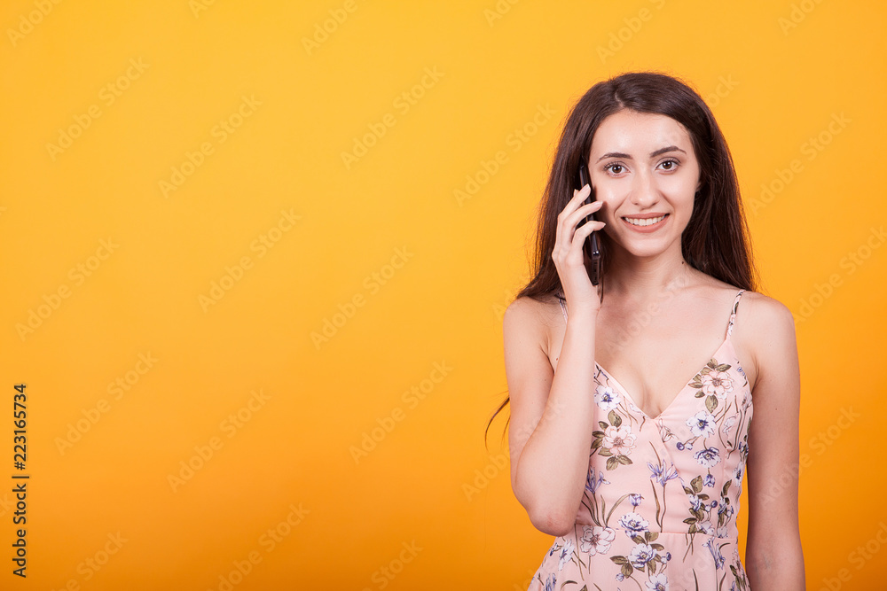 Beautiful young woman talking on her phone in studio over yellow background. Beautiful young woman talking on her phone in studio over yellow background.