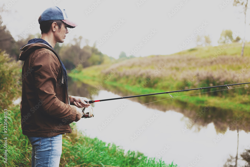 Young fisherman is fishing in river with spinning Young fisherman is fishing in river with spinning