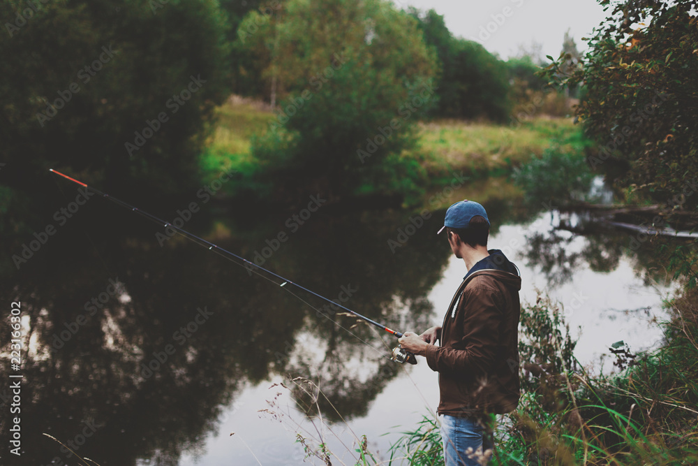 Young fisherman is fishing in river with spinning Young fisherman is fishing in river with spinning