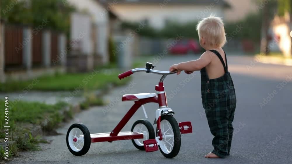 Cute toddler child, boy, playing with tricycle in park and eating apple, kid riding bike on sunset Cute toddler child, boy, playing with tricycle in park and eating apple, kid riding bike on sunset